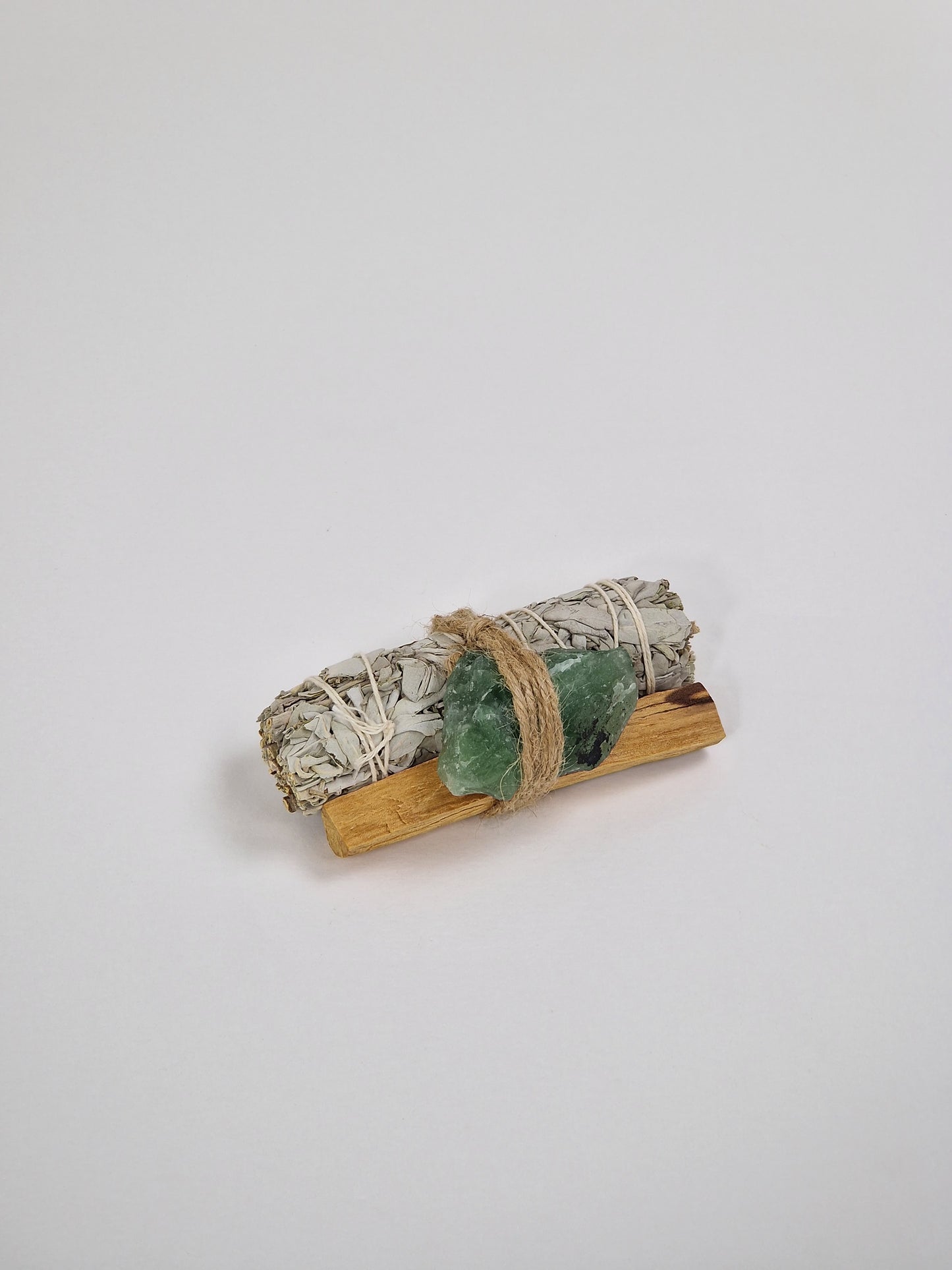 Ein großes Bündel weißer Salbei, ein Stück grüner Fluorit-Rohkristall, grüner Fluoritkristall und ein Stück Palo Santo, heiliges Holz